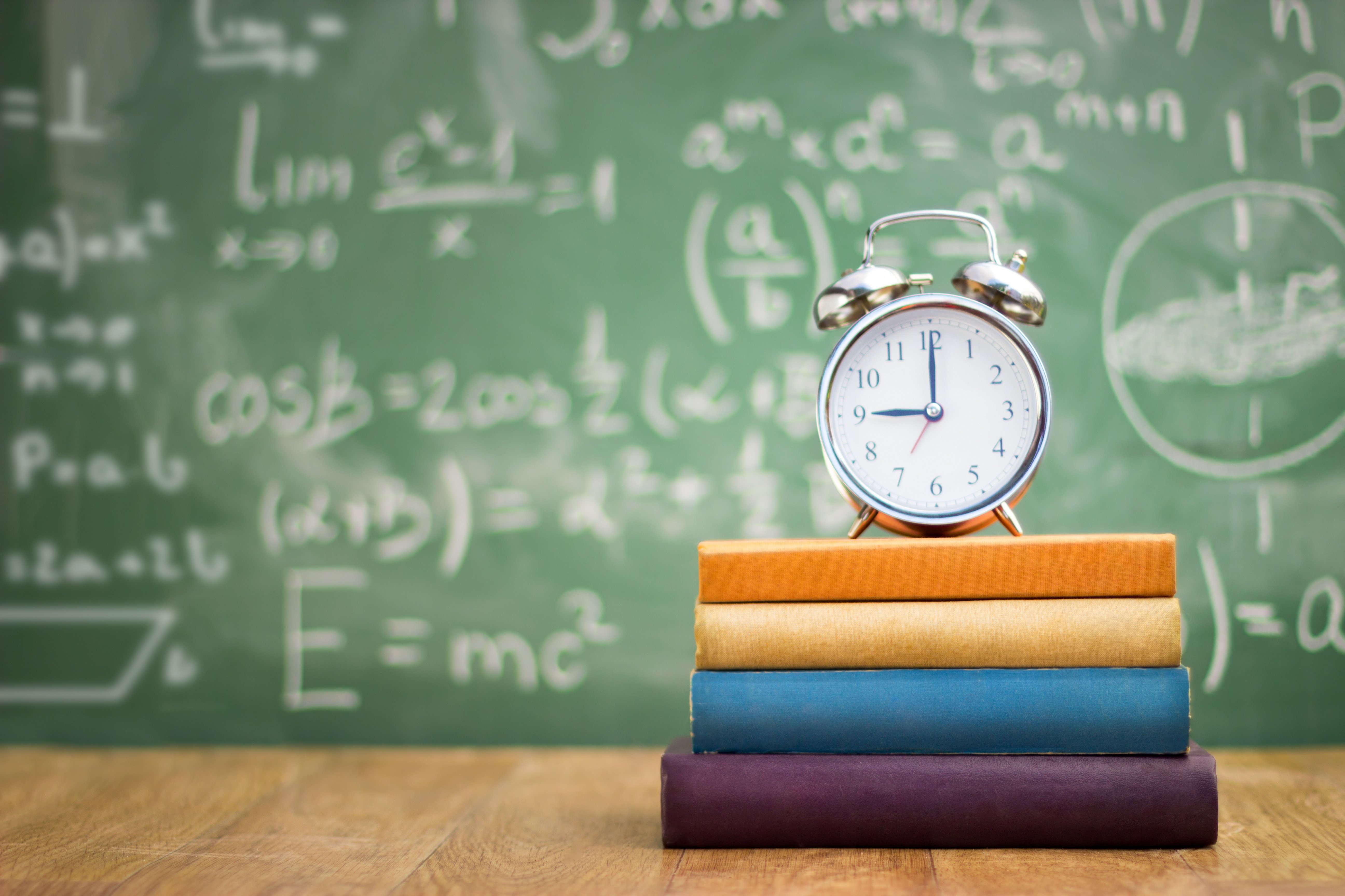 an image of a clock sitting on books in front of a classroom represents flexible learning.