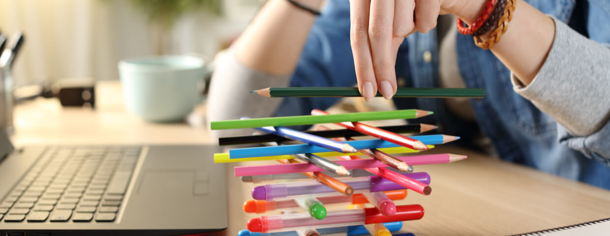 Teen student distracted during online school work, stacking colored pencils in front of open laptop Teen student distracted during online school work, stacking colored pencils in front of open laptop