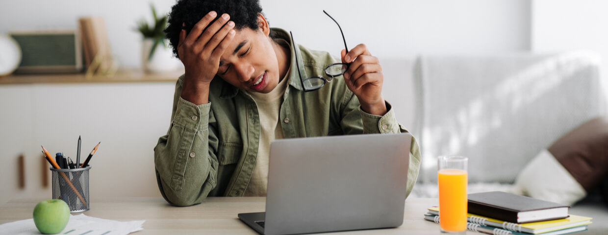 tired teen boy, suffering from headache during online studies in front of laptop at home, exhausted or burned out from online school or homework