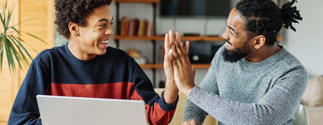 dad giving high schooler high five over laptop dad giving high schooler high five over laptop