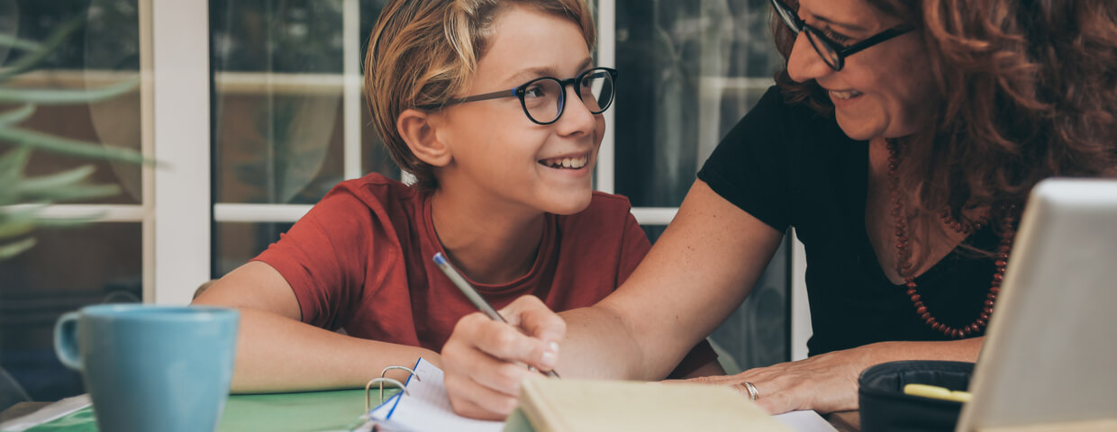 Mom and young son homeschooling, happy, with scchool work and laptop