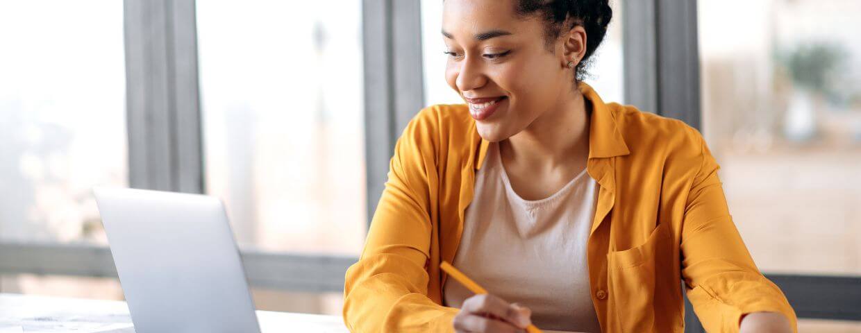 online student taking notes and smiling at screen online student taking notes and smiling at screen