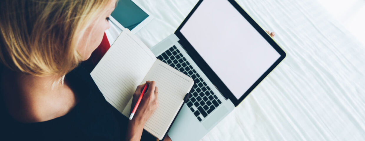 student writing in notebook with laptop