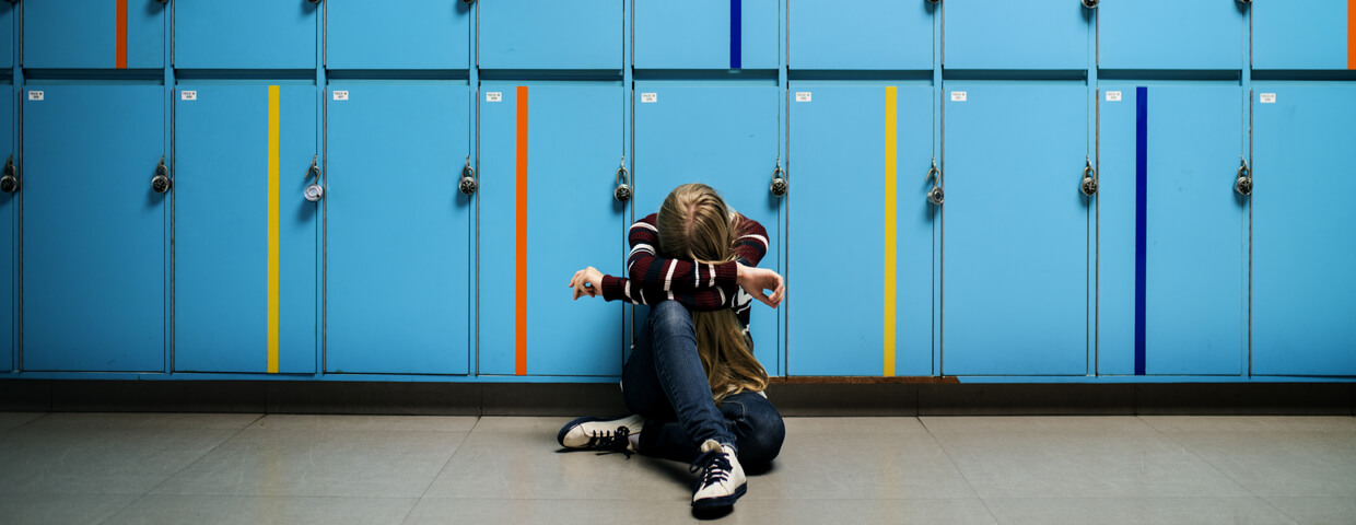 student sitting alone at lockers, young girl with head down at school alone, bullying concept,