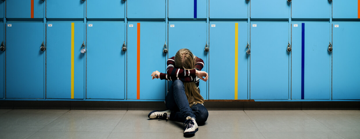 student sitting alone at lockers, young girl with head down at school alone, bullying concept student sitting alone at lockers, young girl with head down at school alone, bullying concept