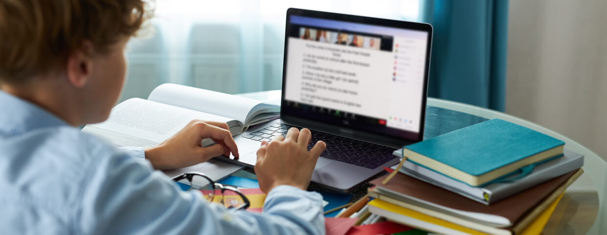 teen boy typing a report or doing schoolwork on a laptop at home, online school or homeschooling concept