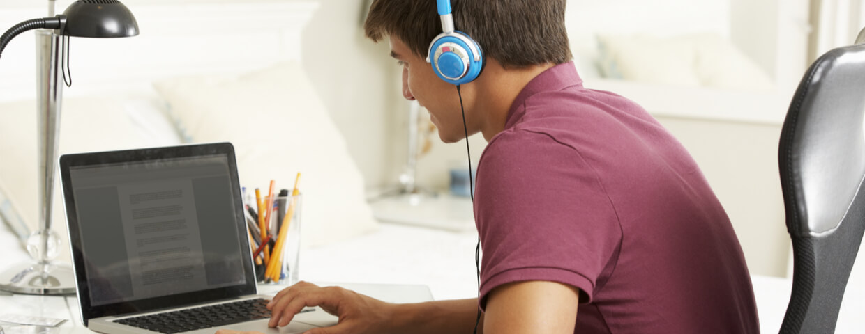 Teenage Boy Studying At Desk In Bedroom Wearing Headphones, Homeschooling concept