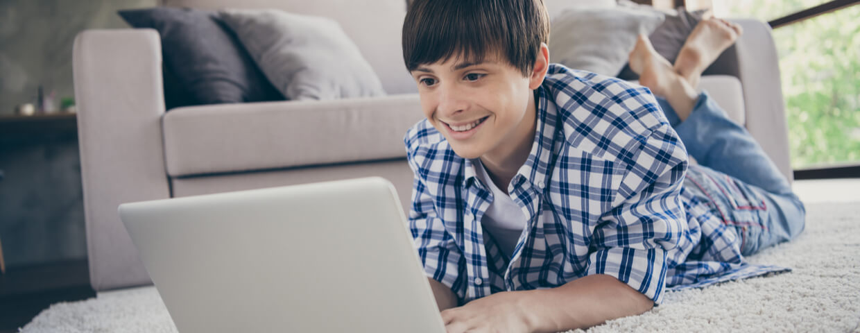 photo of teen boy on the floor doing online school, remote learning, on a laptop