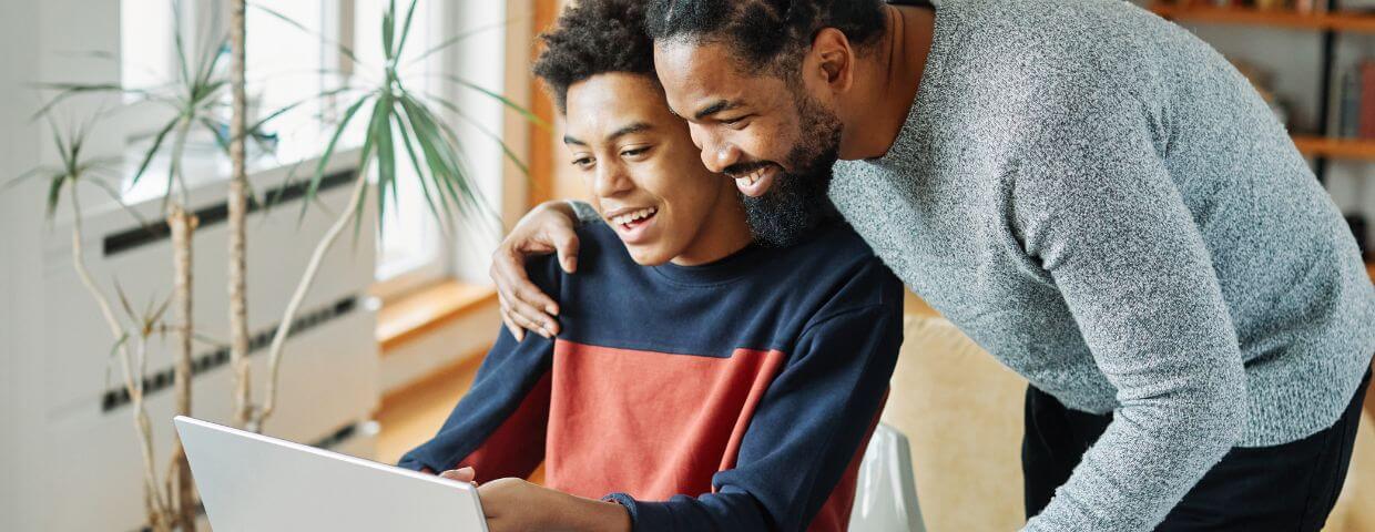 father putting arm around son happily viewing laptop
