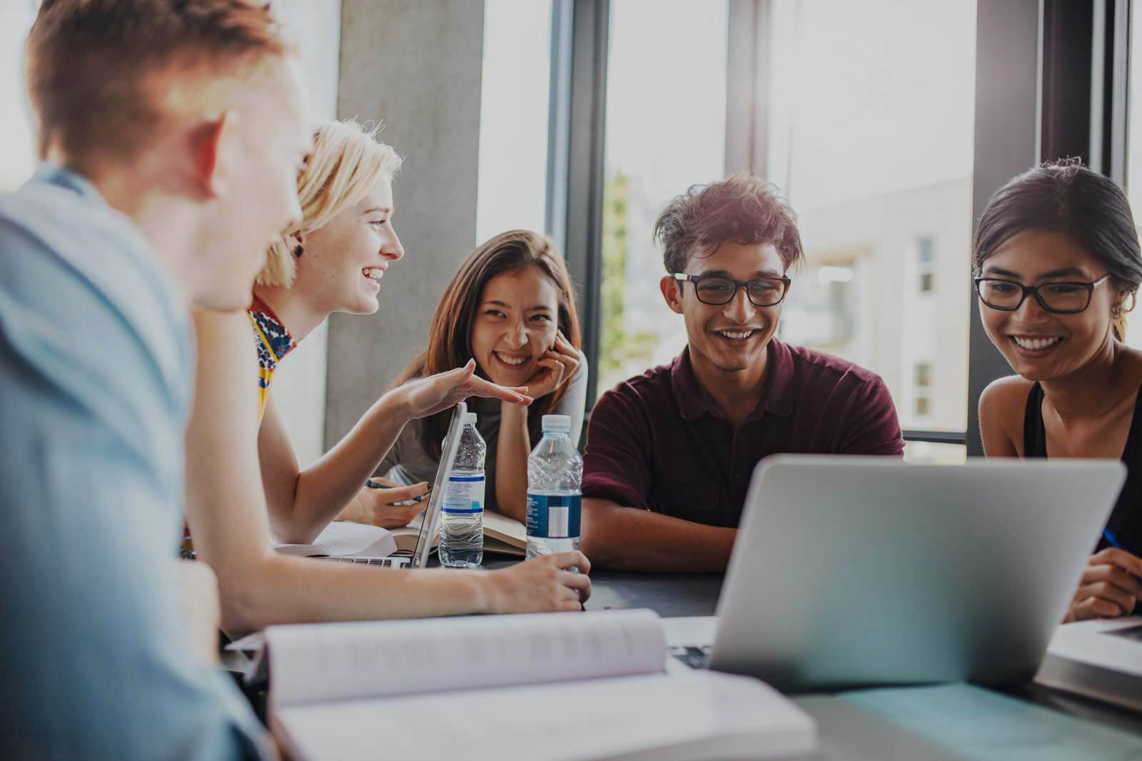 A group of laughing high school students sitting around a large desk