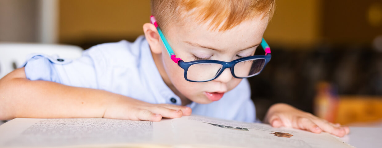Boy with down syndrome with big glasses reading book, homeschool, special education